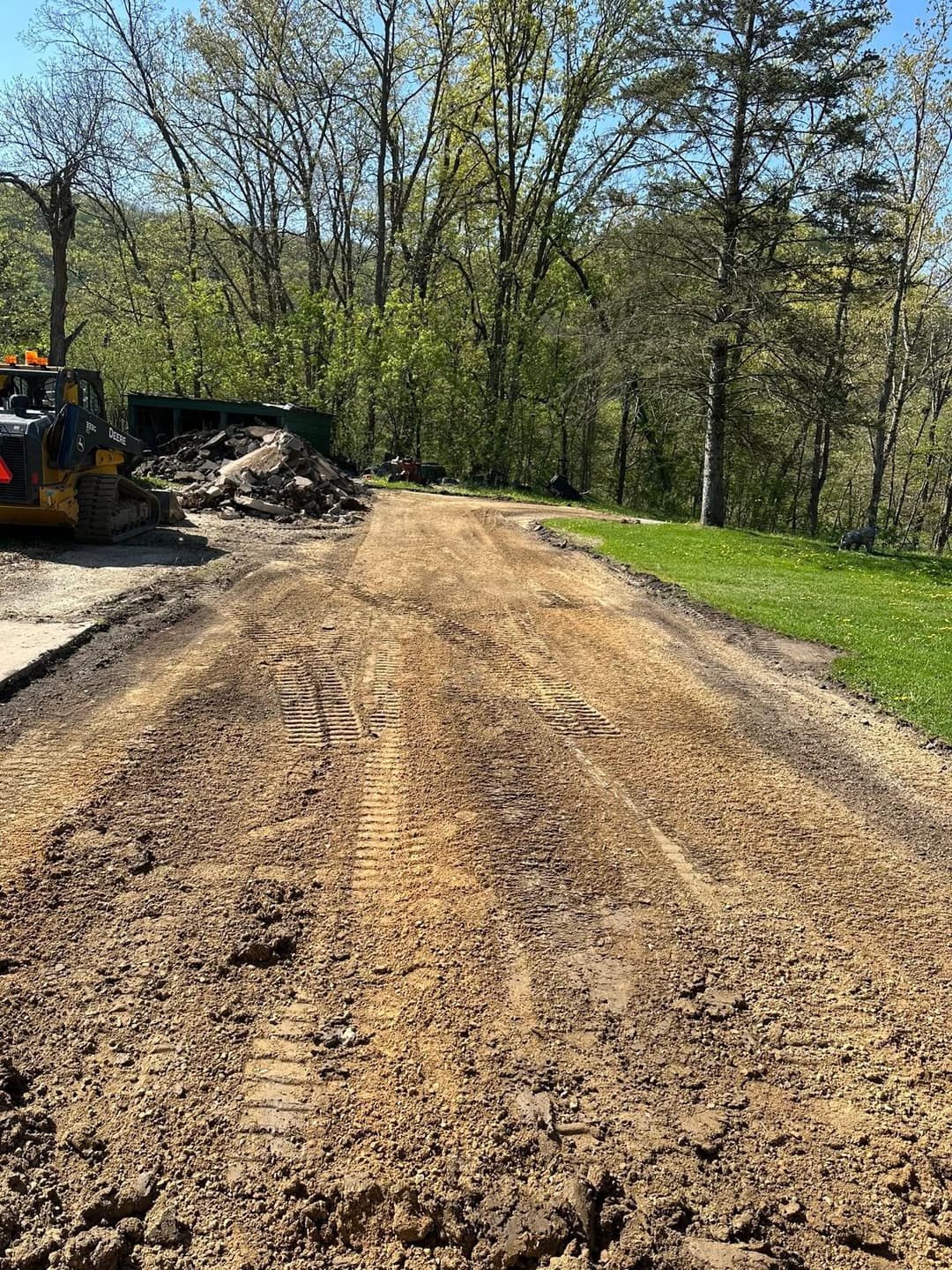 Gravel road construction site with heavy machinery and cleared trees in the background.