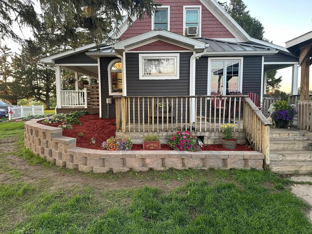 Charming house with vibrant flower garden and landscaped front porch on a green lawn.