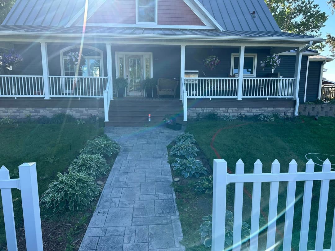 Charming house with a porch, stone path, and lush greenery in a sunny outdoor setting.