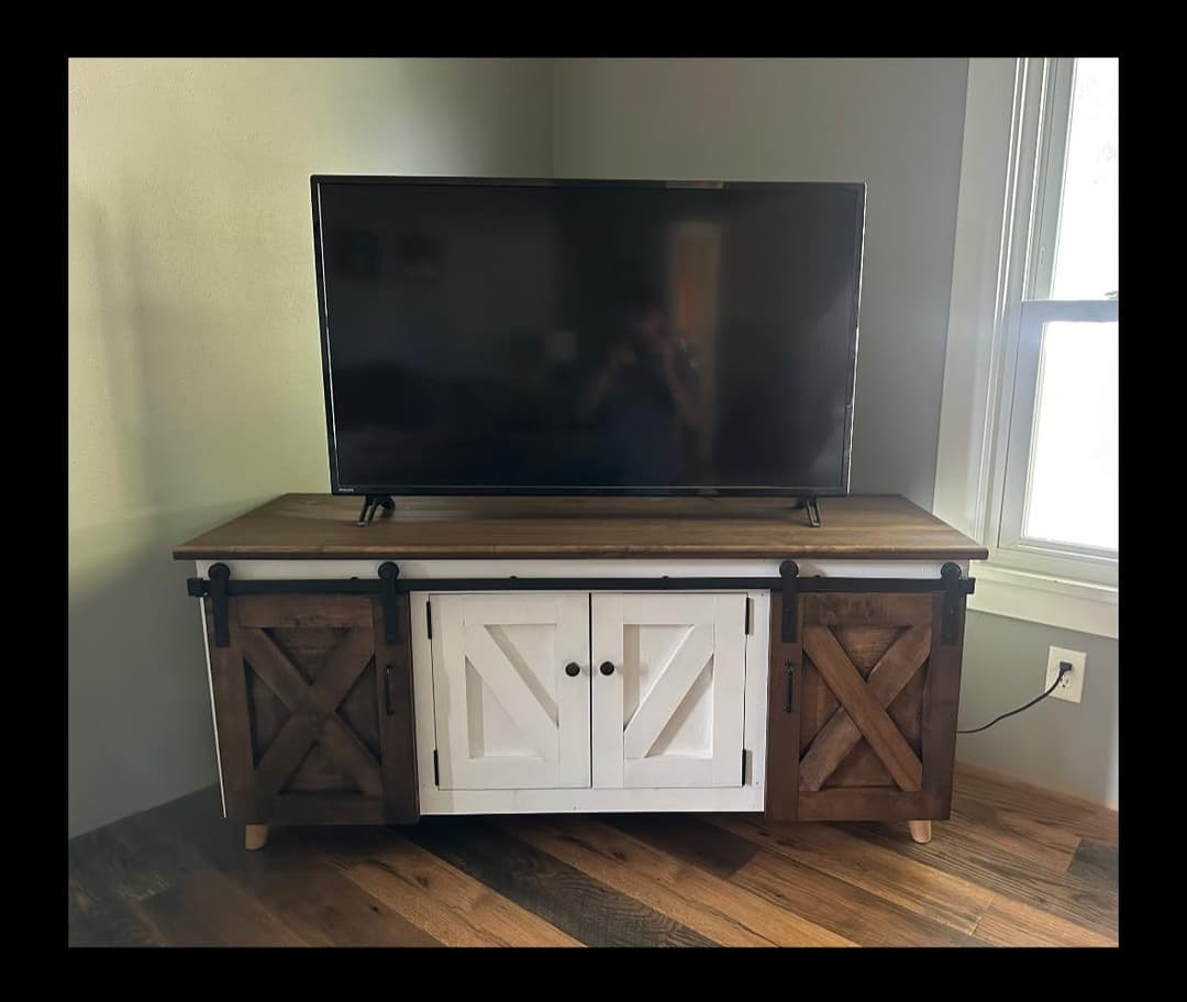 Modern wooden TV stand with barn-style doors, placed near a window in a cozy living room.