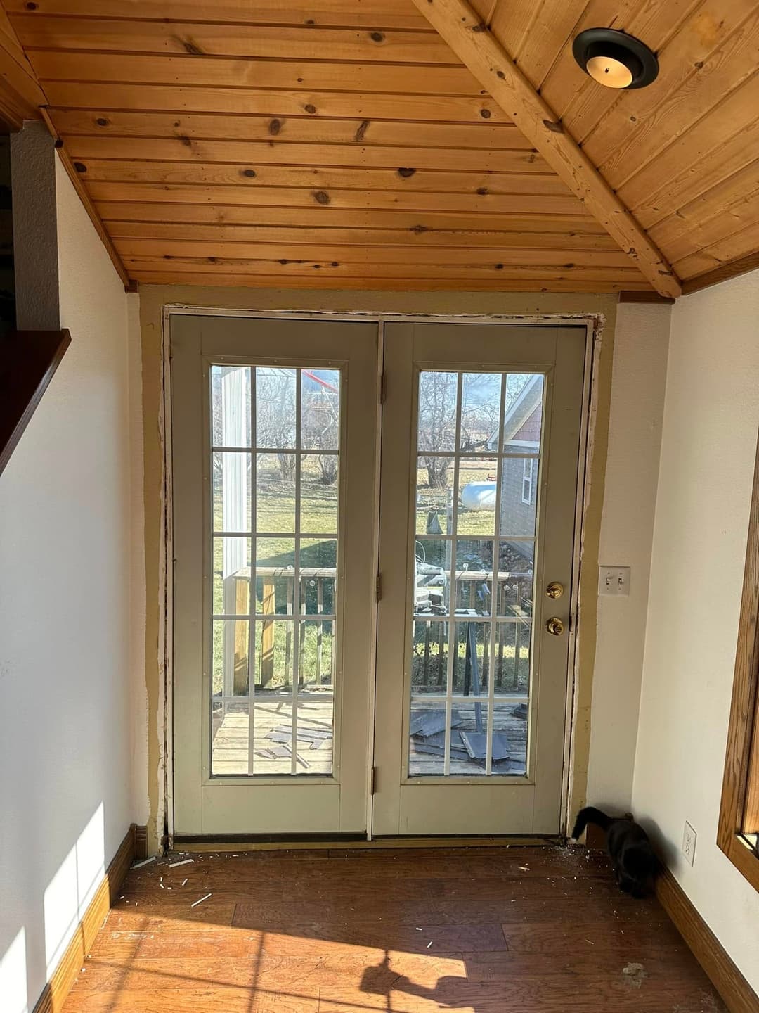 Interior view of double glass doors leading to a deck, featuring wooden paneling and natural light.