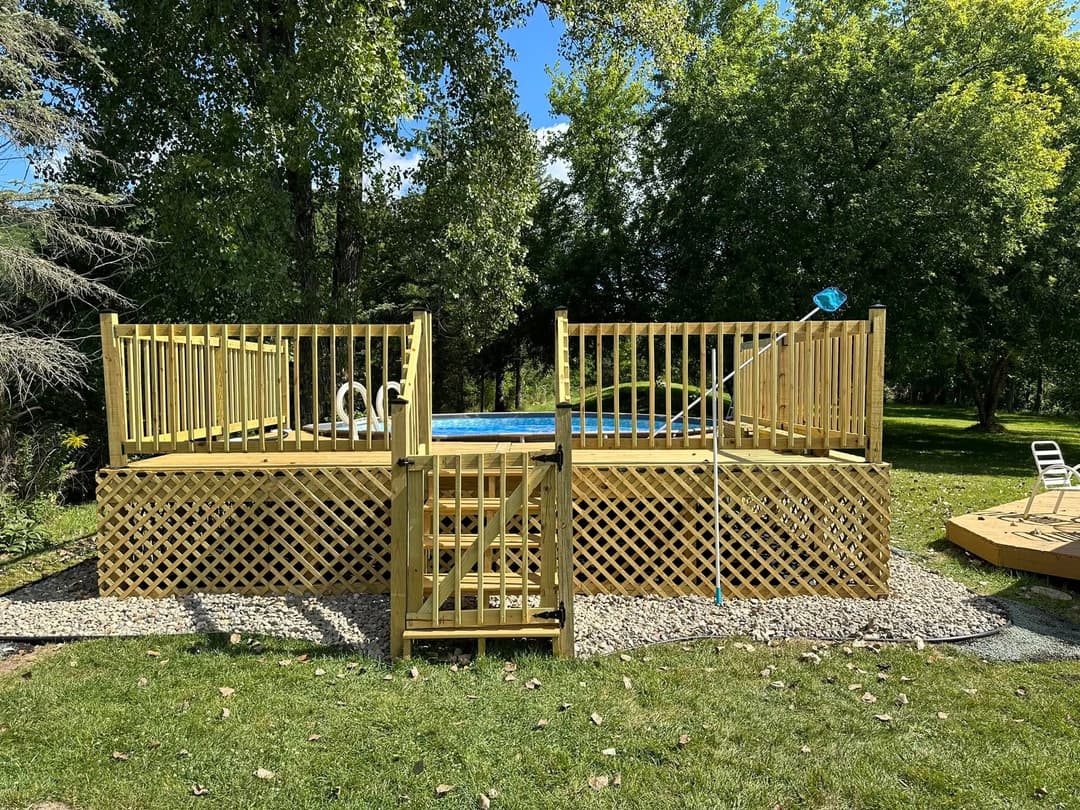 Wooden deck with pool surrounded by greenery, featuring steps and a ladder for easy access.