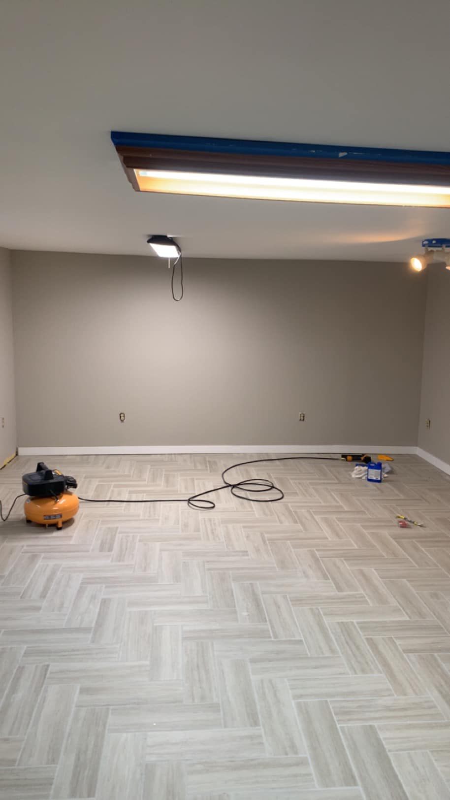Empty room with gray walls, new flooring, paint supplies, and lighting progress visible.