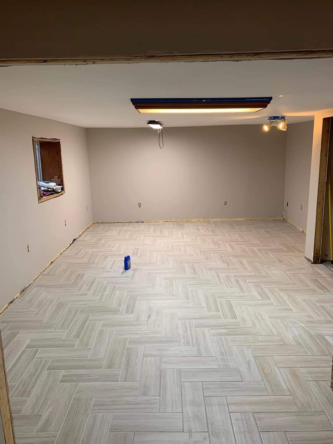 Empty room with light-colored herringbone floor, freshly painted walls, and ceiling lights.