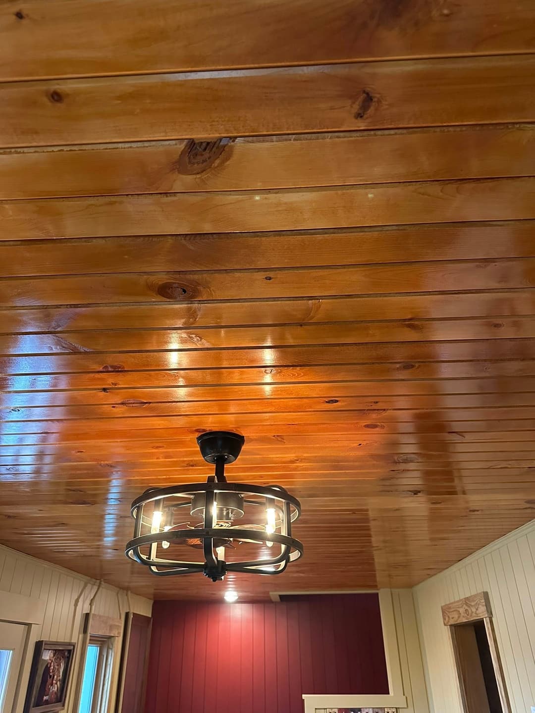 Wooden ceiling with a modern black chandelier in a cozy interior setting.