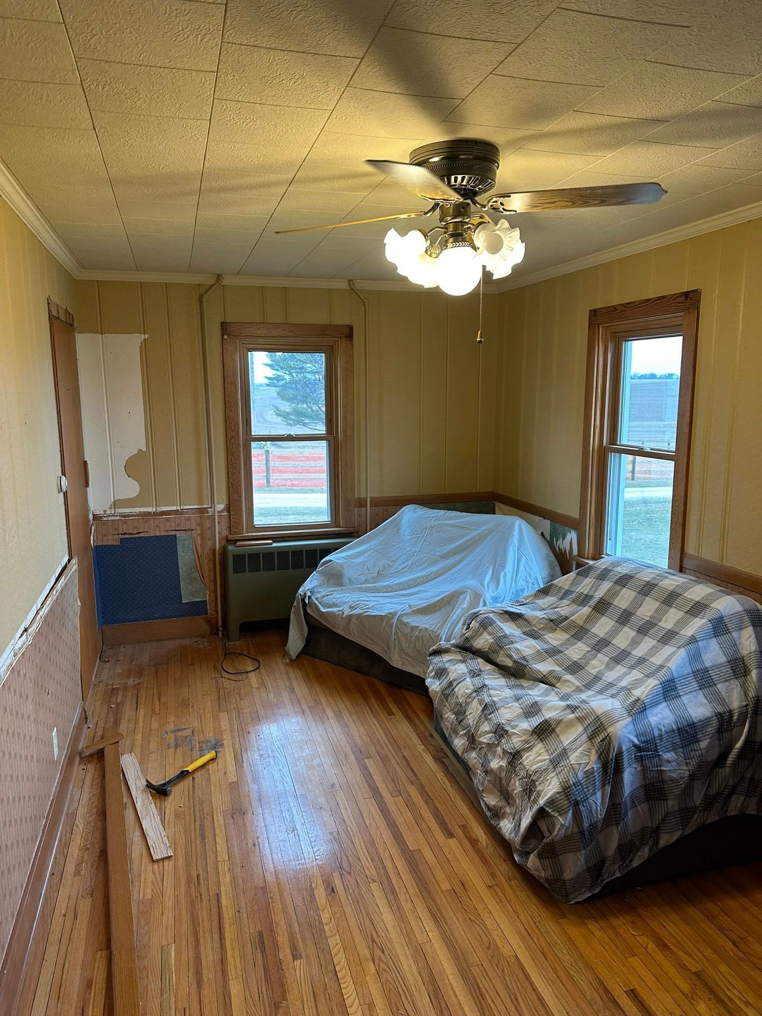 Cozy living room with two covered sofas, wooden floors, and large windows overlooking a field.